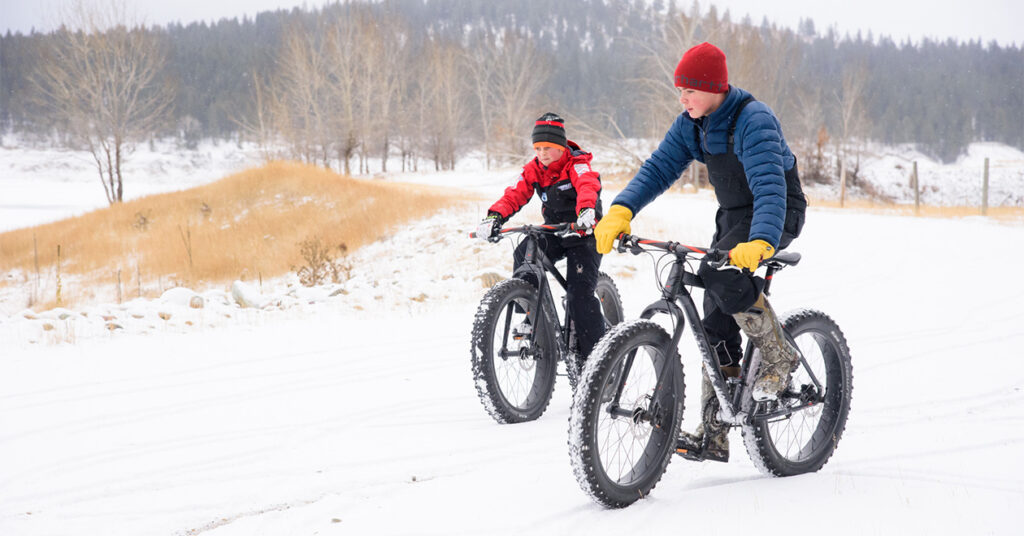 Two kids riding on bikes in the snow
